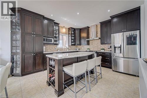Gourmet kitchen featuring dark wood cabinetry, stainless steel appliances, a tiled backsplash, a central island with integrated wine storage, and light-toned tile flooring - 37 Davinci Boulevard, Hamilton, ON 