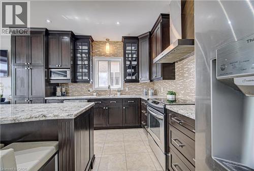 Contemporary kitchen featuring dark wood cabinetry, light granite countertops, a mosaic tile backsplash, and stainless steel appliances - 37 Davinci Boulevard, Hamilton, ON 