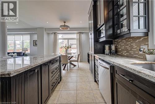 Kitchen featuring dark wood cabinetry, light-colored granite countertops, and a mosaic tile backsplash - 37 Davinci Boulevard, Hamilton, ON 