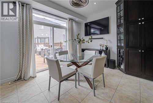 Dining area featuring ceramic tile flooring, built-in dark wood cabinetry with glass fronts, and a full-light sliding glass door opening to a private wood deck - 37 Davinci Boulevard, Hamilton, ON 