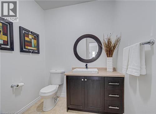Powder room featuring a dark wood-finish vanity with a light-colored countertop, vessel sink with a black faucet, and a round dark-framed mirror - 37 Davinci Boulevard, Hamilton, ON 