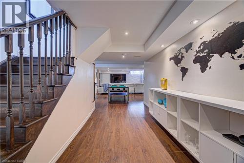 Finished lower level featuring wood-finish flooring, built-in shelving, recessed lighting, and a dark wood staircase with balusters - 37 Davinci Boulevard, Hamilton, ON 