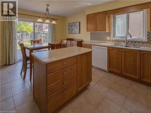 Kitchen featuring wood cabinetry, a center island with drawer storage, a tile backsplash, and a double basin sink - 212 Sleaford Street, Waterloo, ON 