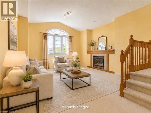 Living area featuring vaulted ceilings, a large arched window, a fireplace with a wood mantel, and carpeted stairs with wood railing - 212 Sleaford Street, Waterloo, ON 