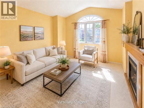 Spacious living area featuring a prominent arched window, a fireplace with a wood mantle, and soft carpeting - 212 Sleaford Street, Waterloo, ON 