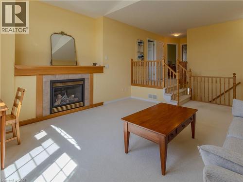 Living area featuring a gas fireplace with a wood mantle and tile surround, light-toned carpeting, and natural wood railings - 212 Sleaford Street, Waterloo, ON 