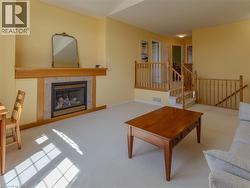 Living area featuring a gas fireplace with a wood mantle and tile surround, light-toned carpeting, and natural wood railings - 