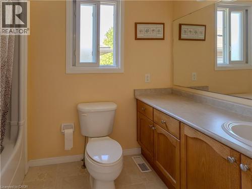 Bathroom featuring a single window, a built-in wood-finish vanity with a single basin, a full-width mirror, a white toilet, and tiled flooring - 212 Sleaford Street, Waterloo, ON 