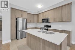 Modern kitchen featuring light wood-finish cabinetry, stainless steel appliances, a center island with an undermount double basin sink, and white countertops - 
