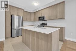 Contemporary kitchen featuring light wood-finish cabinetry, stainless steel appliances, and a central island with a white countertop - 