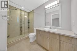 Contemporary bathroom featuring a spacious glass-enclosed shower with decorative tile inlay, a single vanity with a light-toned countertop, a rectangular framed mirror, and tile flooring - 