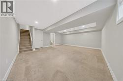 Spacious carpeted room featuring a staircase with carpeted treads, a white paneled door, recessed lighting, and a window - 
