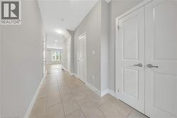 Hallway featuring light-toned tile flooring, neutral wall paint, white baseboards, and multiple white panel doors with brushed nickel hardware - 