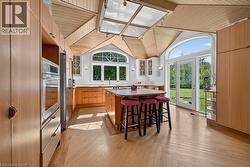 Kitchen featuring wood-finish cabinetry, a central island with a contrasting countertop, integrated appliances, and light wood-finish flooring in a herringbone pattern - 
