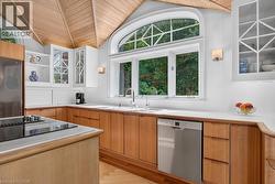 Kitchen featuring a vaulted wood-paneled ceiling, white upper cabinetry with glass inserts, wood-finish lower cabinetry, and a large arched window above the sink - 
