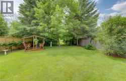 Expansive backyard featuring a manicured lawn, established trees, and a wooden gazebo structure - 