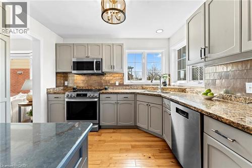Kitchen featuring light-toned cabinetry, granite countertops, stainless steel appliances, a tile backsplash, and wood-finish flooring - 26 Shadyridge Place, Kitchener, ON 