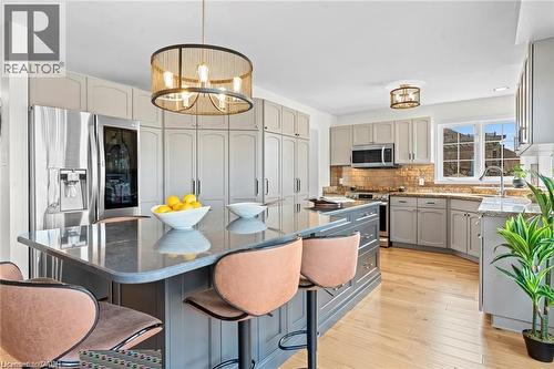 Kitchen featuring a spacious island with seating, stainless steel refrigerator, light gray cabinetry, wood-finish flooring, and a window above the sink - 26 Shadyridge Place, Kitchener, ON 