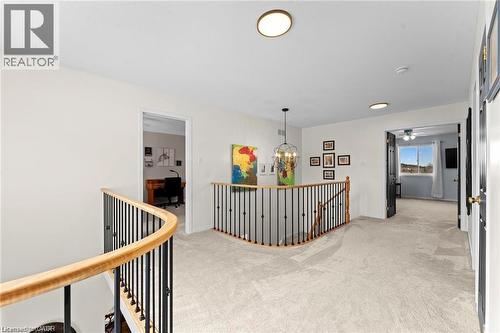 Carpeted upper-level hallway featuring a curved wood and iron railing, a chandelier, and multiple flush-mount ceiling lights - 26 Shadyridge Place, Kitchener, ON 
