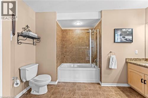 Bathroom featuring a tub and shower combination with glass enclosure, a vanity with a granite-style countertop, light wood cabinetry, and a white toilet - 26 Shadyridge Place, Kitchener, ON 