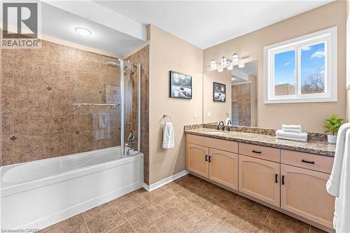 Bathroom featuring a bathtub with a glass shower enclosure, a dual vanity with a granite countertop, wood-finish cabinetry, and tiled flooring - 26 Shadyridge Place, Kitchener, ON 