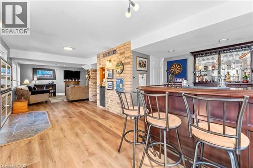Spacious entertainment area featuring wood-finish flooring, a full-service bar with built-in cabinetry and glass storage, an exposed brick accent wall, and recessed lighting - 26 Shadyridge Place, Kitchener, ON 