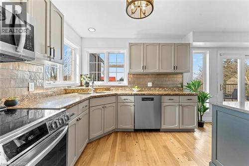 Modern kitchen featuring light-toned cabinetry, granite-style countertops, stainless steel appliances, a stone-look tile backsplash, and wide-plank wood-finish flooring - 26 Shadyridge Place, Kitchener, ON 