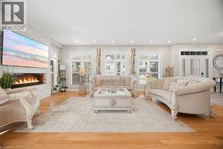 Bright living area featuring wood-finish flooring, a linear fireplace with a textured surround, and multiple windows with plantation shutters - 