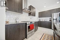 Contemporary kitchen featuring dark wood-finish cabinetry, speckled countertops, stainless steel appliances, a geometric tile backsplash, and light-toned tile flooring - 