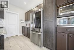 Kitchen featuring wood-finish cabinetry, stainless steel refrigerator, light-toned tile flooring, and integrated built-in appliances - 