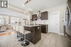 Kitchen featuring a large island with a stone-finish countertop, dark wood cabinetry, stainless steel appliances, and a decorative tile backsplash - 