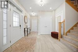 Foyer featuring a white entry door with decorative glass inserts and sidelights, light-toned tile flooring, recessed lighting, and a staircase with light wood newel posts and black metal balusters - 
