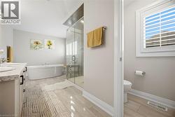 Spacious bathroom featuring a freestanding soaking tub, a large glass-enclosed shower, dual vanity with undermount sinks and light-toned countertops, and light wood-finish flooring - 