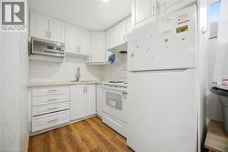Compact kitchen featuring white cabinetry, a stainless steel microwave, a white electric range, a white refrigerator, and wood-finish flooring - 