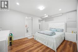 Bedroom featuring wood-finish flooring, recessed lighting, and a white paneled headboard - 