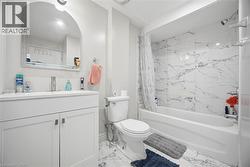 Full bathroom featuring a white vanity with a rectangular basin, an arched mirror, and white tiled flooring - 