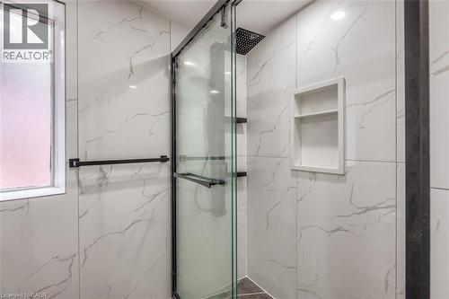 Shower enclosure featuring a frameless glass door, black matte fixtures, a rain showerhead, a built-in shower niche, and large format marble-look tile walls - 41 Springhurst Avenue, Toronto, ON 