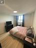 Bedroom featuring wood-finish flooring, a broad window with vertical blinds and dark curtains, and a flush-mount ceiling light fixture - 225 Harvard Place Unit# 1505, Waterloo, ON 
