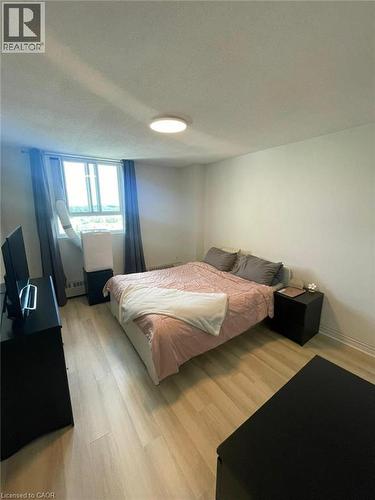 Spacious room featuring wood-finish flooring, white walls, and a large window with privacy curtains - 225 Harvard Place Unit# 1505, Waterloo, ON 