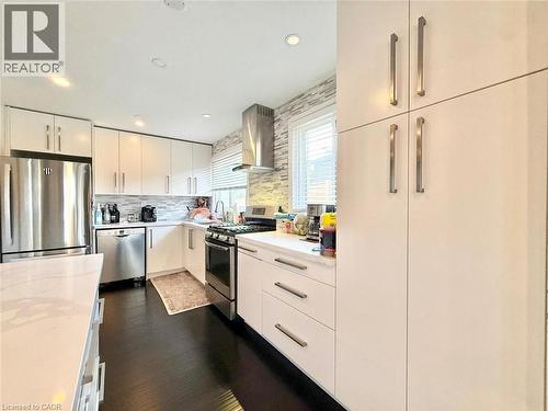 Modern kitchen featuring white cabinetry, dark wood-finish flooring, stainless steel appliances, a stacked tile backsplash, and recessed lighting - 3135 Palmer Drive, Burlington, ON 