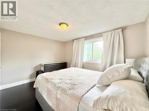 Bedroom featuring dark wood-finish flooring, light neutral-toned walls, a single window with white trim, and a ceiling-mounted light fixture - 3135 Palmer Drive, Burlington, ON 