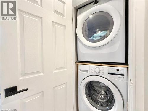 Integrated laundry station featuring a white stackable washer and dryer, a wood-finish platform, and a paneled door with a matte black lever handle - 3135 Palmer Drive, Burlington, ON 