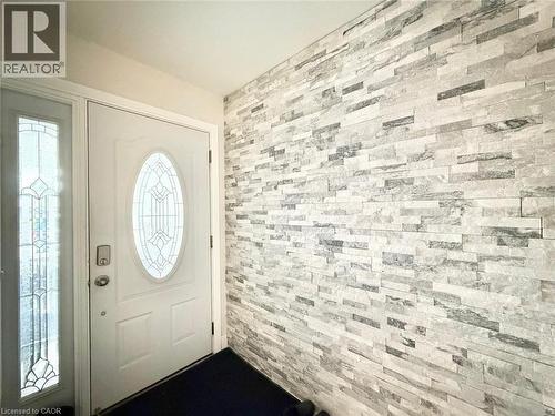 Entryway featuring a white door with decorative oval glass insert, sidelight with leaded glass, and an accent wall with stacked stone tile - 3135 Palmer Drive, Burlington, ON 