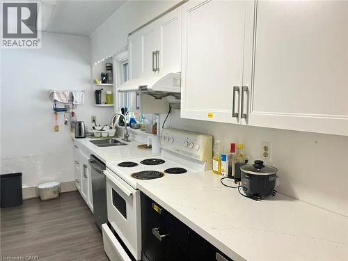 Kitchen featuring white shaker-style cabinetry with brushed nickel hardware, white stone-finish countertops, stainless steel sink, and wood-finish flooring - 110 Peppler Street, Waterloo, ON 