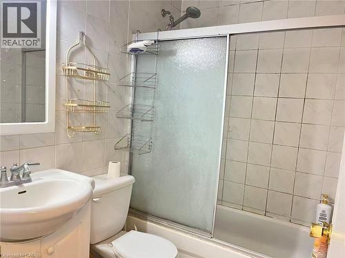 Bathroom featuring a white ceramic vanity sink, a toilet, a bathtub with a sliding frosted glass enclosure, and square tile walls - 110 Peppler Street, Waterloo, ON 
