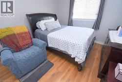 Wood-finish flooring throughout, featuring a window with horizontal blinds and drapery panels, and a dark wood dresser with multiple drawers - 