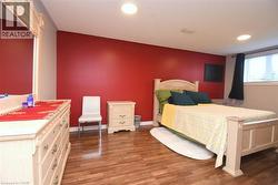 Bedroom featuring wood-finish flooring, a vibrant accent wall, recessed lighting, and a window with blinds - 
