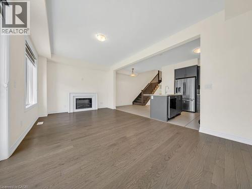 Spacious living area featuring wood-finish flooring, a fireplace with a white mantel, and ample natural light from large windows - 76 Grassbourne Avenue, Kitchener, ON 