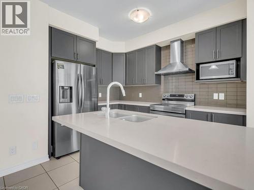 Modern kitchen featuring gray cabinetry, stainless steel appliances, a white single-basin sink with a gooseneck faucet, light-toned countertops, and a tiled backsplash - 76 Grassbourne Avenue, Kitchener, ON 