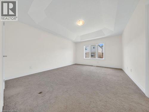 Spacious room featuring a tray ceiling, flush-mount lighting, broad baseboards, gray carpet, and a multi-pane window - 76 Grassbourne Avenue, Kitchener, ON 